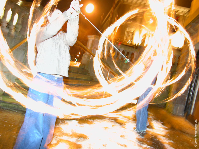 A person in a pale top spins fire poi at night, with bright circular trails of light