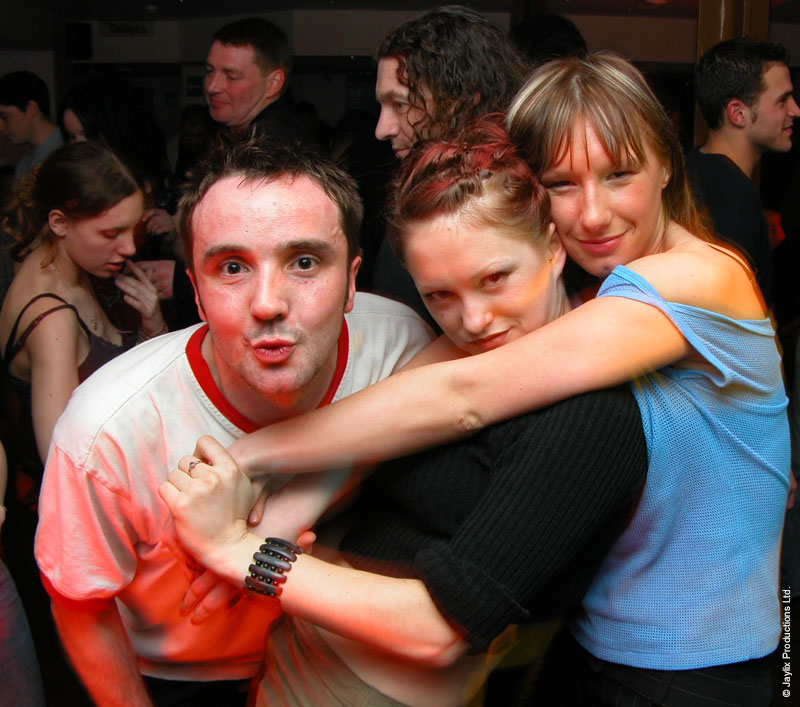 Three people hug and pull faces for the camera in a busy bar