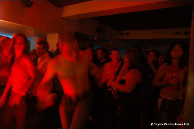 A dark, red-lit crowd on a dance floor, with a shirtless person near the centre