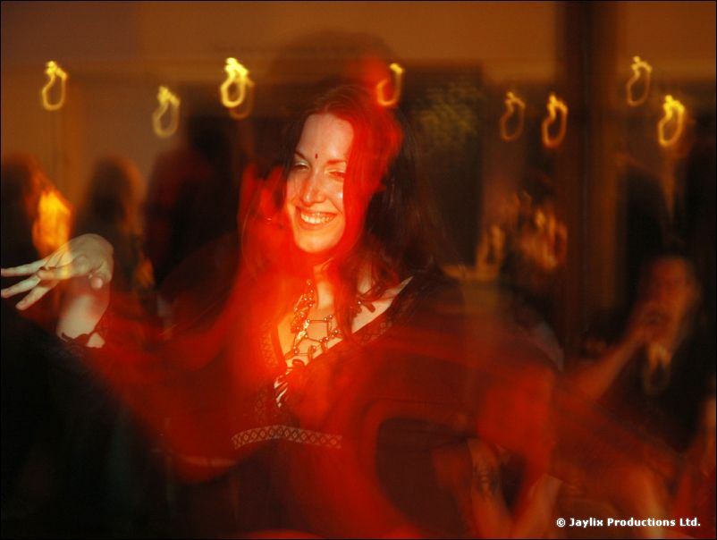 A smiling woman with dark red hair in a red-lit, blurred bar with light streaks