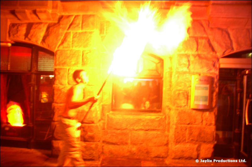 A person breathes fire against a stone building wall, everything tinted orange