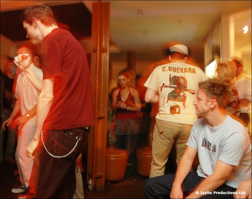 People in a room, a man in a red t-shirt with a chain, another in a C. Guevara t-shirt and cap