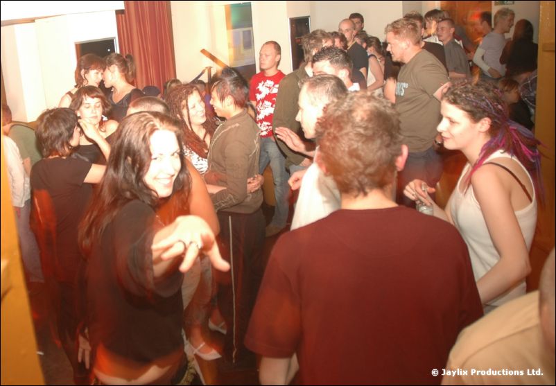 A crowd of dancers in a room, a woman with long dark hair reaching toward the camera
