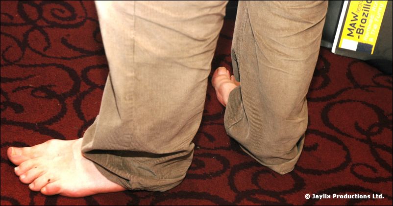 A bare foot on a patterned red carpet beside khaki trousers