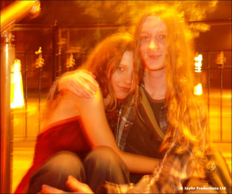 Two people hug in orange street light, one with long hair