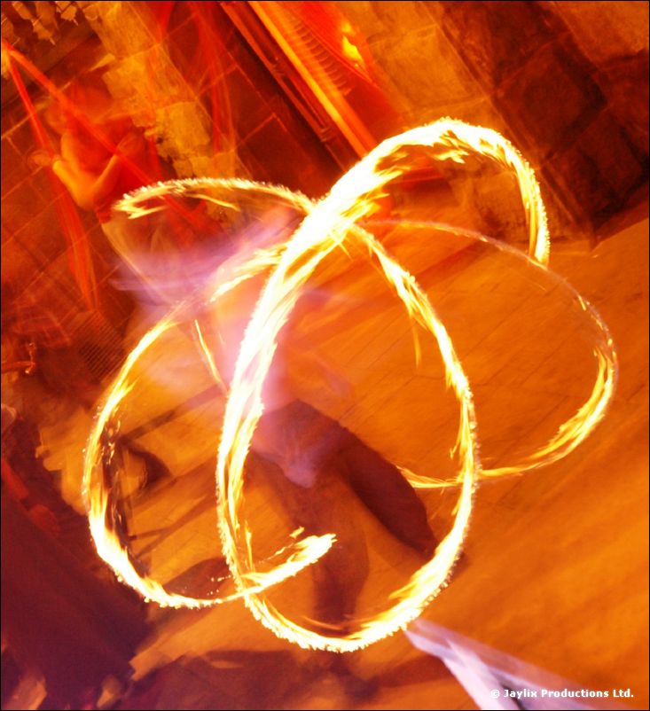 Blurred rings of fire spun by a person in a stone-paved street at night