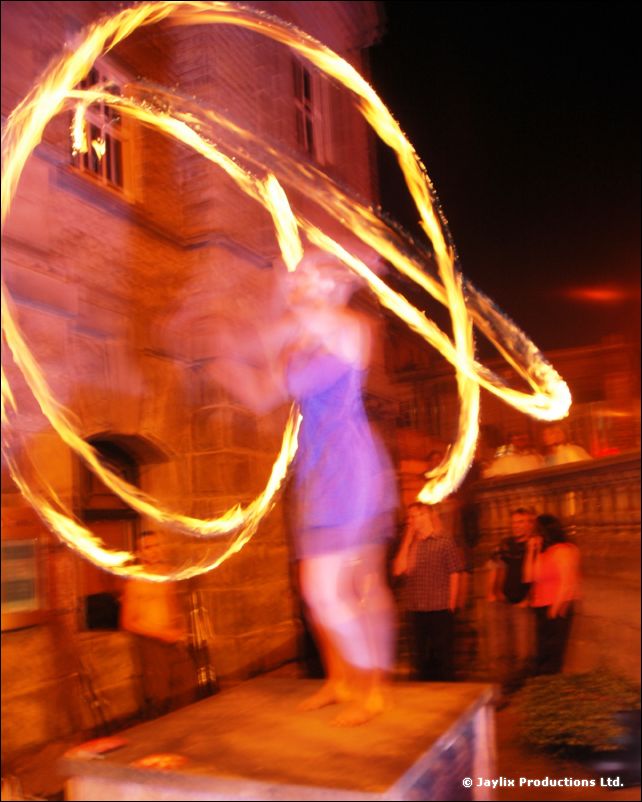A person on a table spinning rings of fire in front of a stone building at night