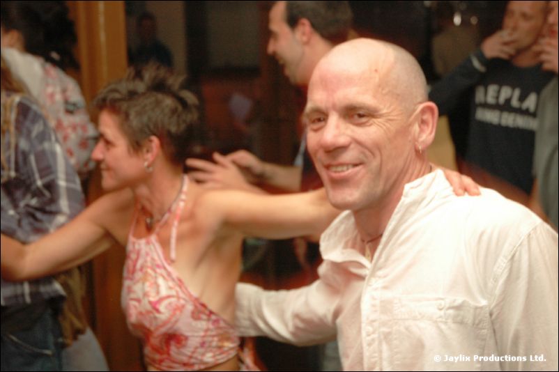 A bald man in a white shirt smiles beside a woman dancing in a crowd