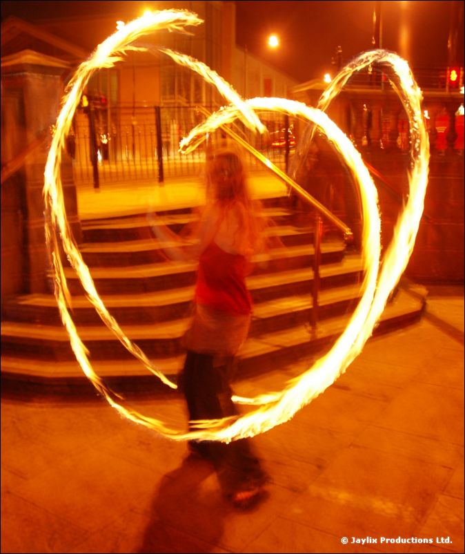 A woman spins rings of fire in front of steps and railings at night