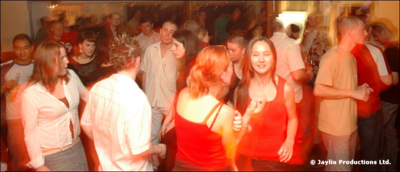 People dancing in a busy bar, two women in red tops at the front