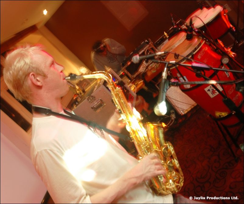 A man plays a saxophone beside red conga drums