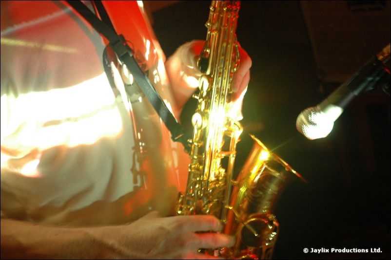 Close-up of a saxophone and a microphone, with a person in a pale top behind