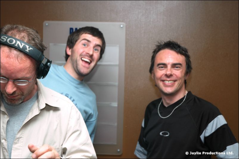 Three men at DJ decks, one in headphones, smile in front of a Bar Med sign