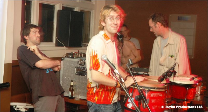 A man in an orange flame-print shirt plays congas while three people stand behind him
