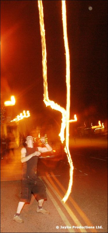 A person swings two long streaks of fire in a dark street