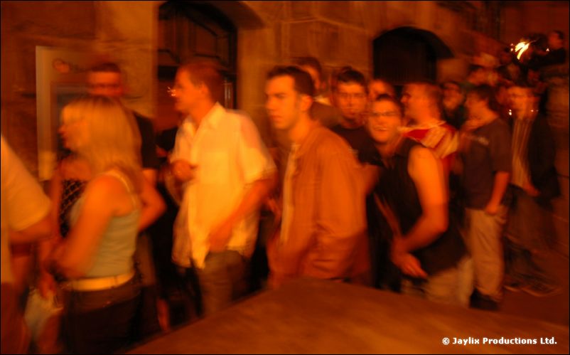 People stand in a queue for a nightclub at night outside a stone building
