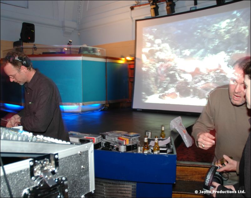 A man with headphones works at a mixing desk by a screen showing an underwater scene