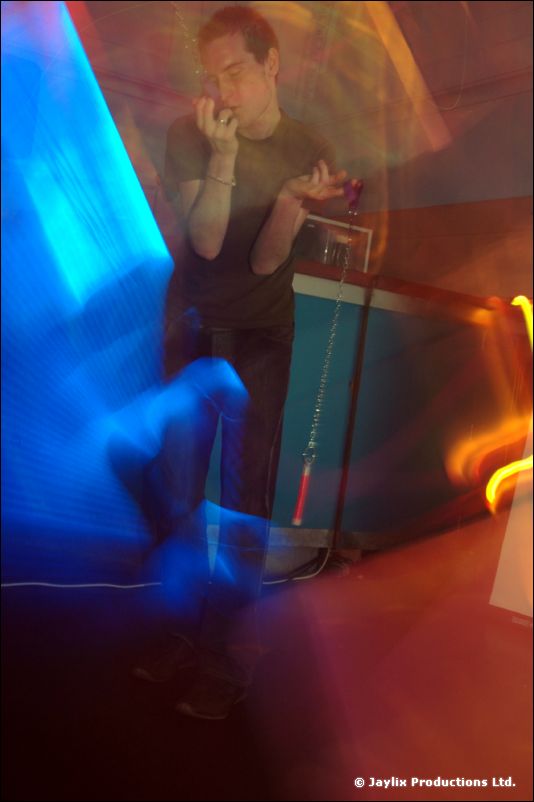 A blurred person cups their hands to their mouth by a blue-lit DJ booth