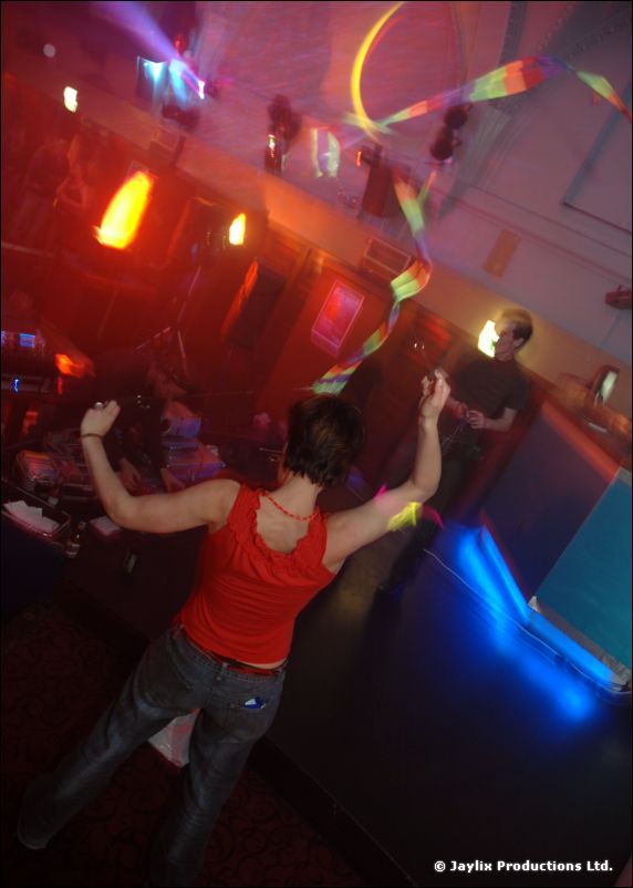 A person in a red top dances with raised arms by a blue-lit stage, rainbow ribbon above