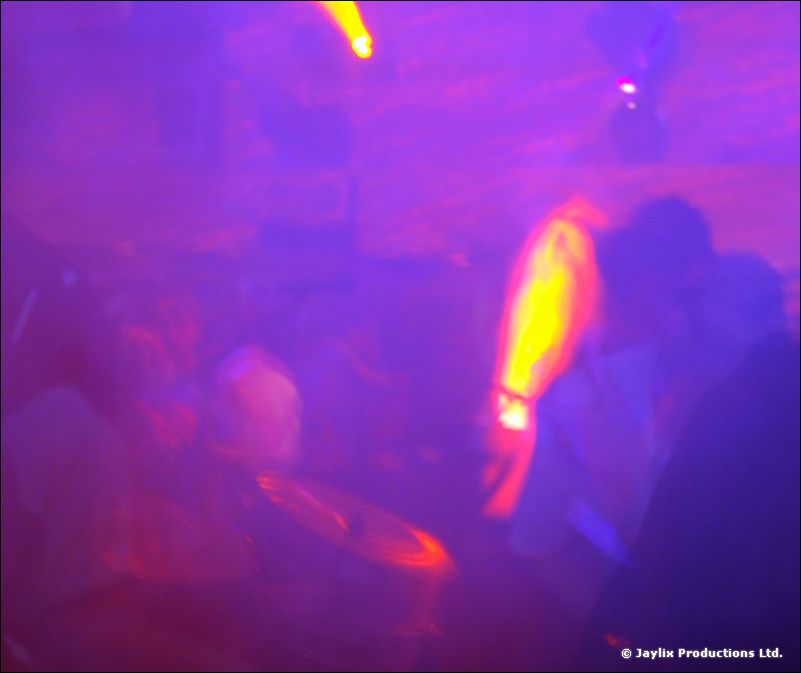 Blurred purple-lit scene with a bright flame effect and dark figures