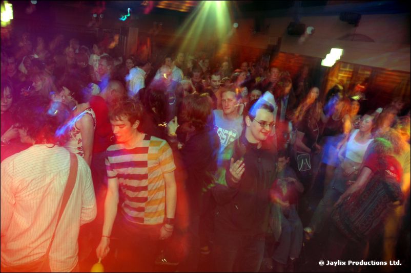 A packed dance floor under green and red lights, with a person in a striped top in front