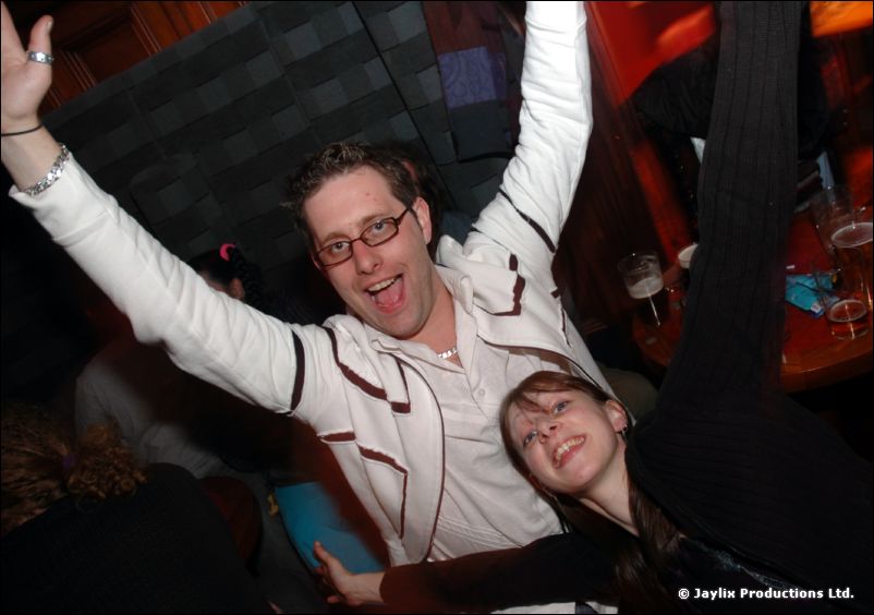 A man with glasses throws his arms up beside a smiling person lying next to him