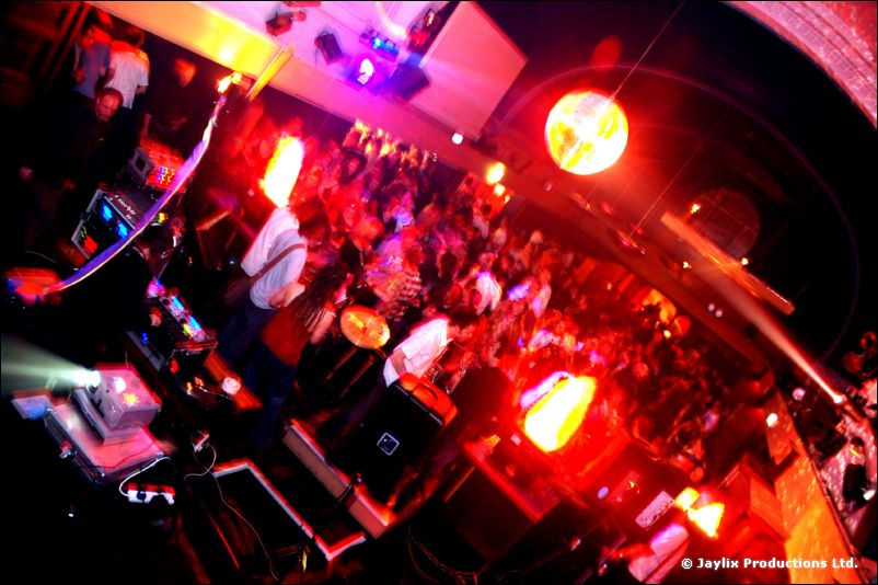 Wide-angle view of a band and a packed crowd with a mirror ball and glowing flame units