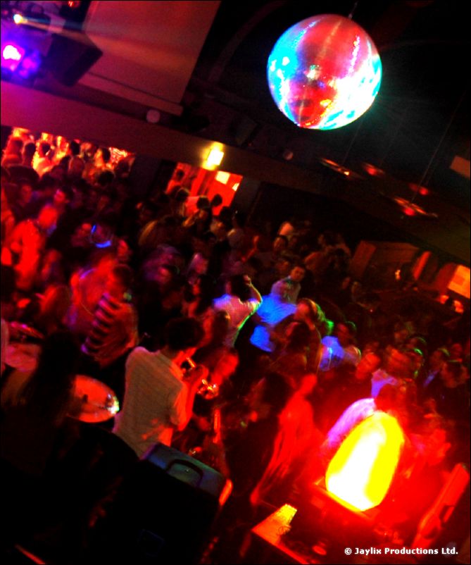 Wide-angle view of a crowd below a mirror ball, with a glowing flame unit at the bottom