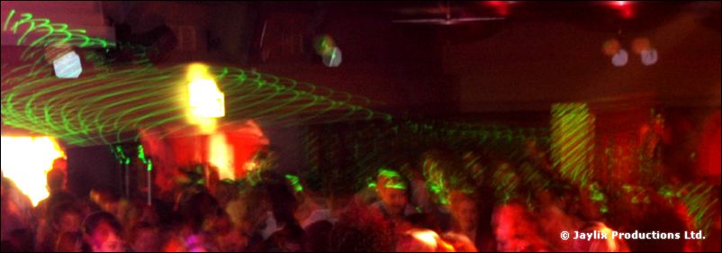 Panoramic view of a dark crowded room with green laser lines and orange flame effects
