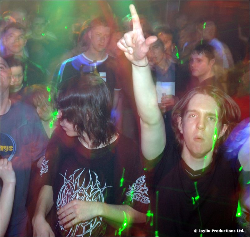 A young man raises his arm in a crowd lit by green laser dots, another dancer beside him