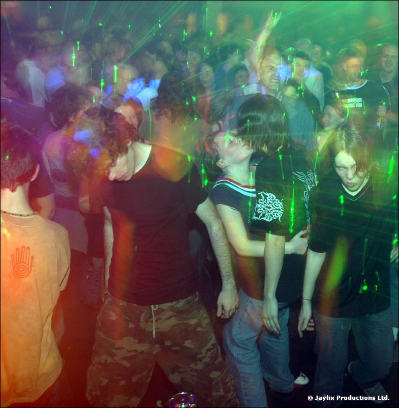 Dancers in dark T-shirts sway in a crowd under green laser light