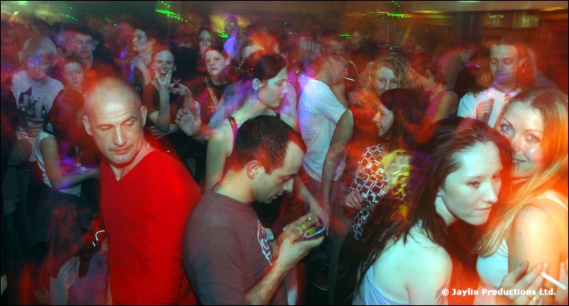 Crowded dance floor with a man in a red top and women smiling near the camera