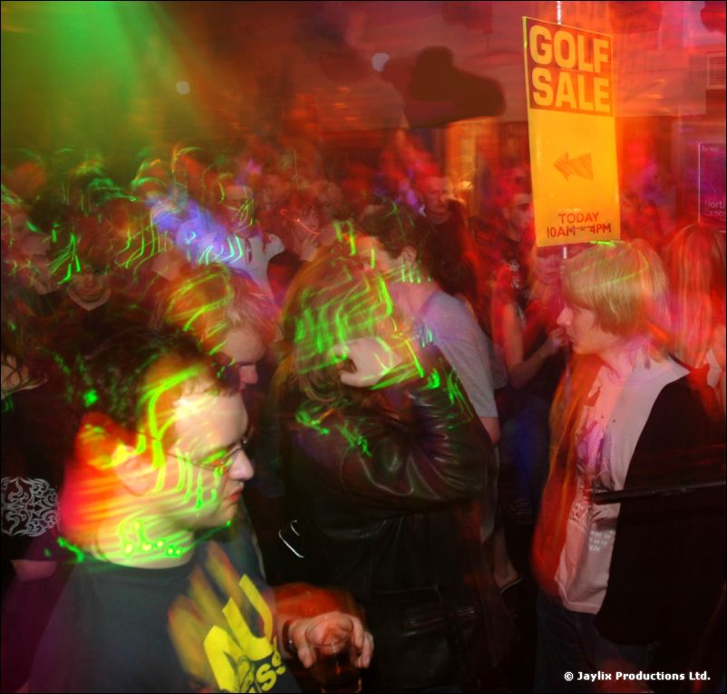 Dancers in a crowd with green laser patterns and a yellow Golf Sale sign above