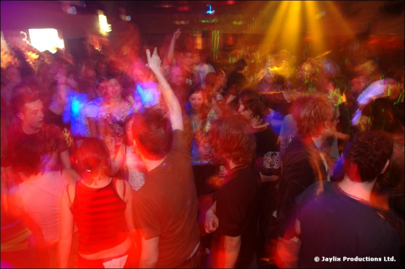 Dancers in a crowd lit with orange and yellow light, one person raising a hand