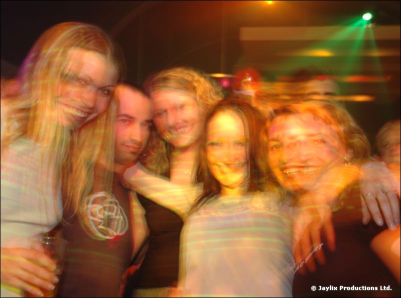 Five people smile close together with arms around each other, lit in warm colours