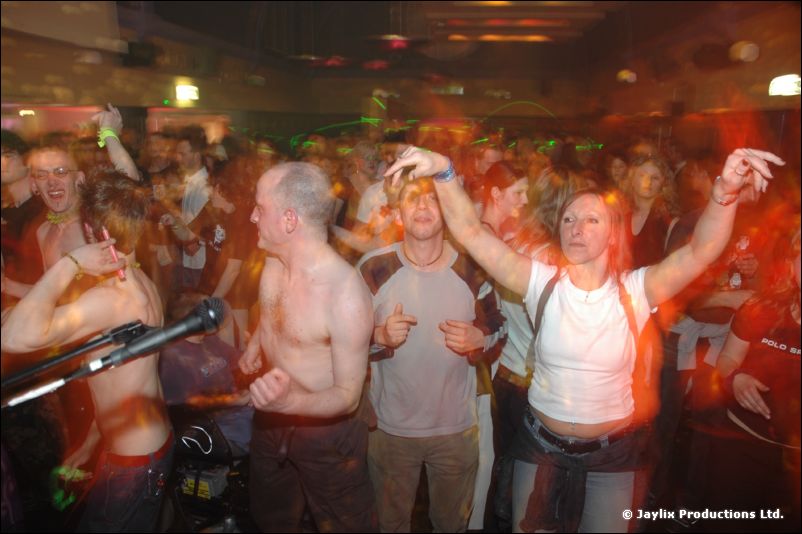 A crowd dances near a microphone, with shirtless men and a woman raising her arms