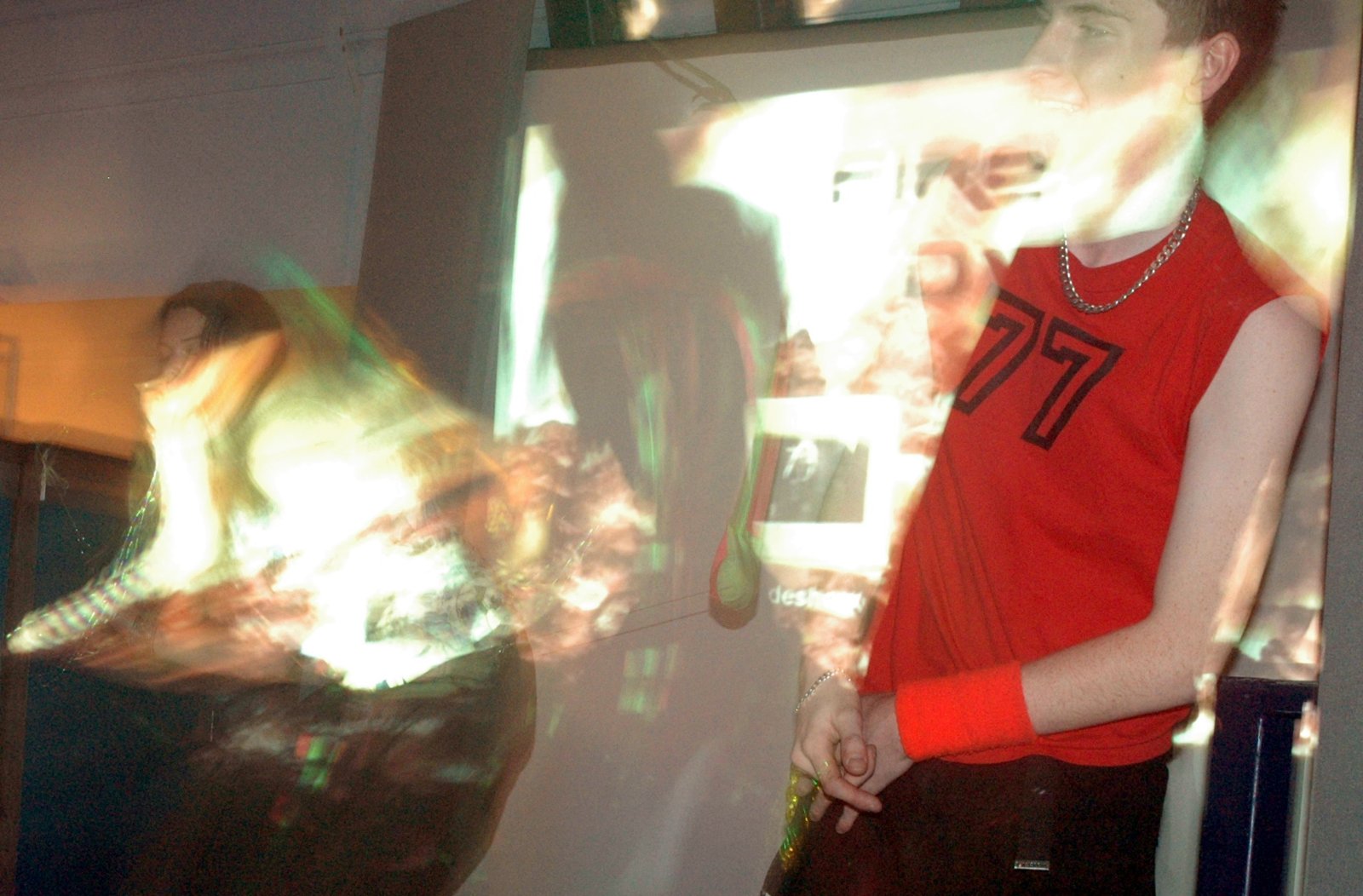 A blurred person in a red number 77 top stands in front of a bright projected image