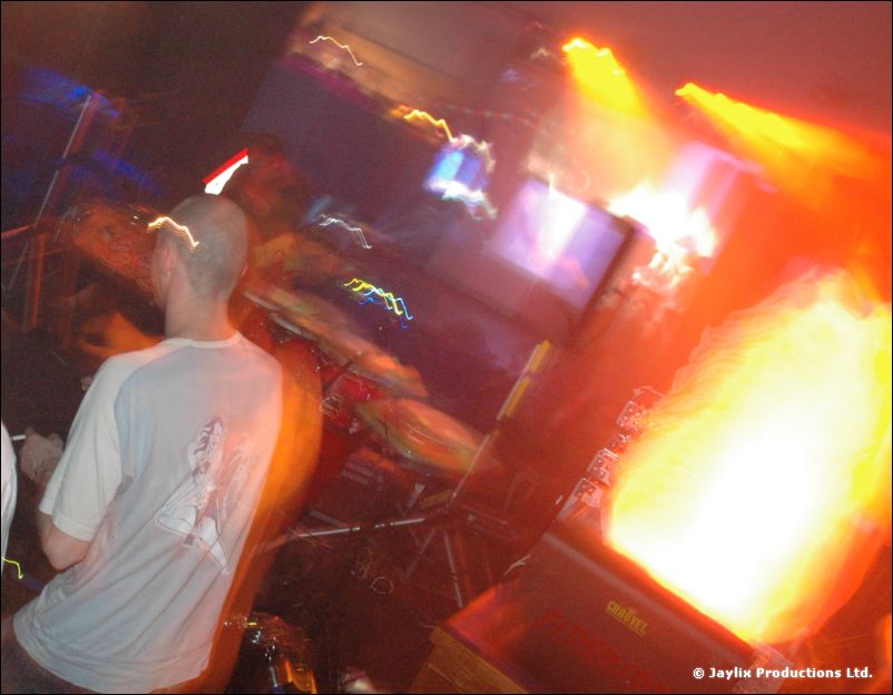 A person in a grey T-shirt stands by a drum kit next to a bright orange flame effect