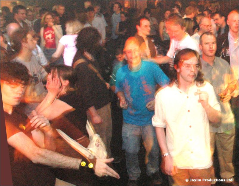 A crowd dances close together, with a person in a white shirt and a person in a blue T-shirt in front