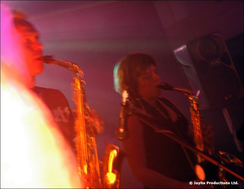 Two saxophone players perform, lit in pink and purple