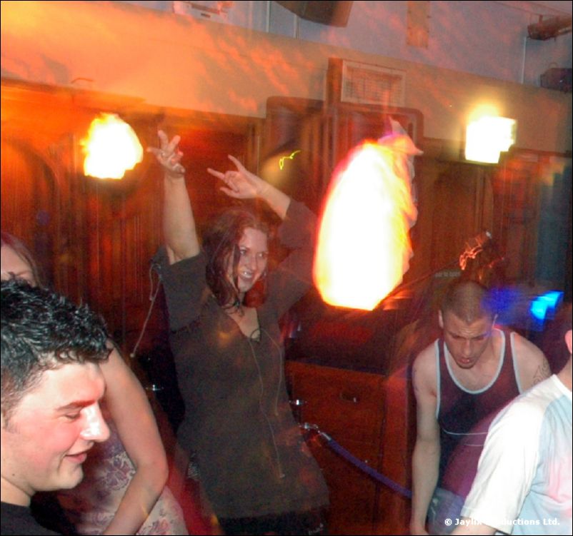 People dance in front of a glowing flame effect, a woman raising her arm in the centre