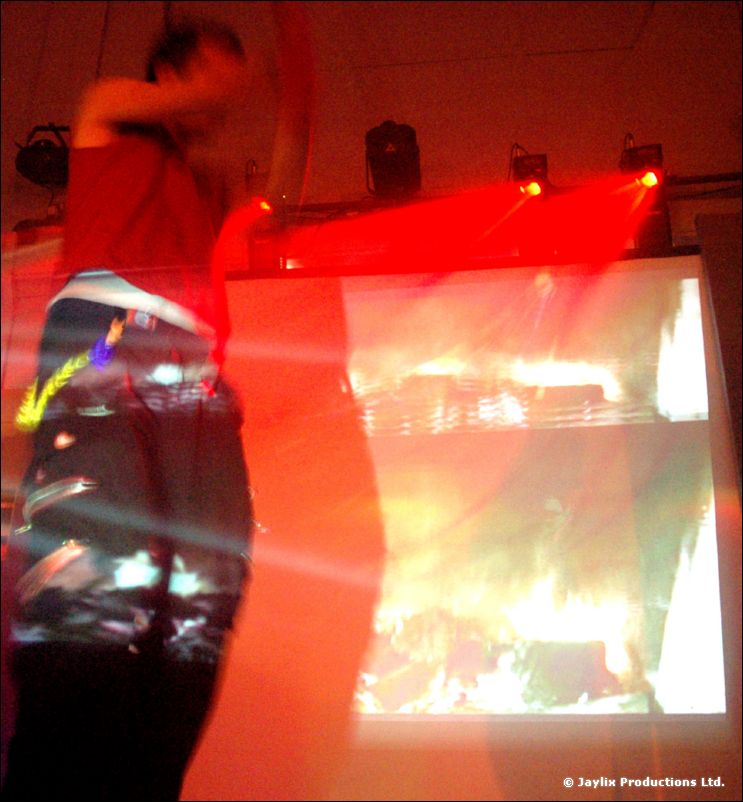 A blurred person in a red top stands before a screen of projected flames under red light