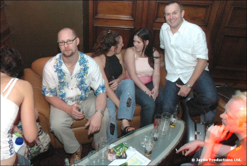 A group sits on a sofa and chairs around a low table with drinks in a bar