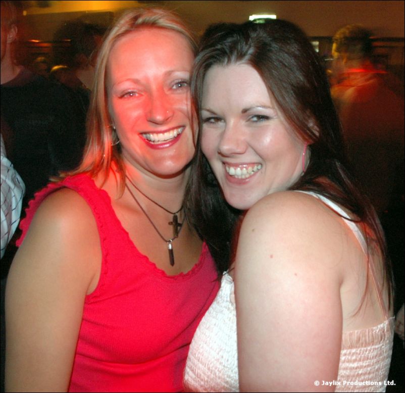 Two women smile at the camera, one in a red top and one in a white top