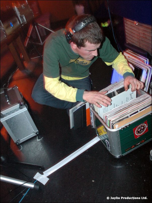 A DJ with headphones crouches over a crate of vinyl records