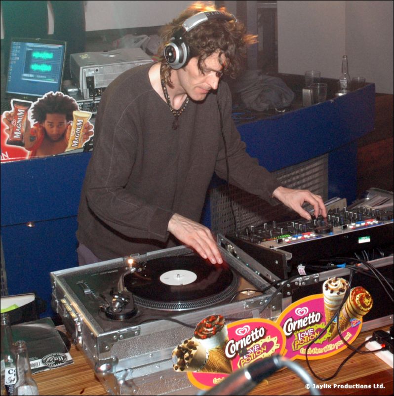 A curly-haired DJ with headphones mixes at turntables beside Cornetto ice cream stickers