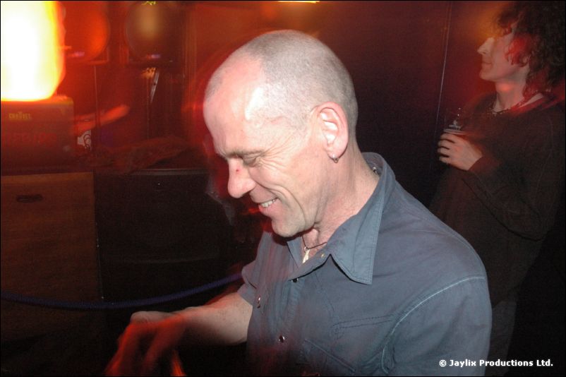 A bald smiling man in a grey shirt looks down in a dimly lit room
