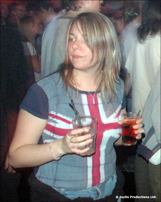 A woman in a Union Jack T-shirt holds a drink in a crowd