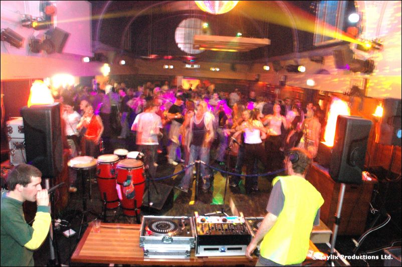 High view of a crowded dance floor with lights, red congas and DJ decks, two people in the foreground