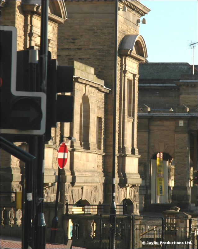 Stone buildings and a traffic light on a sunlit street, with a no entry sign